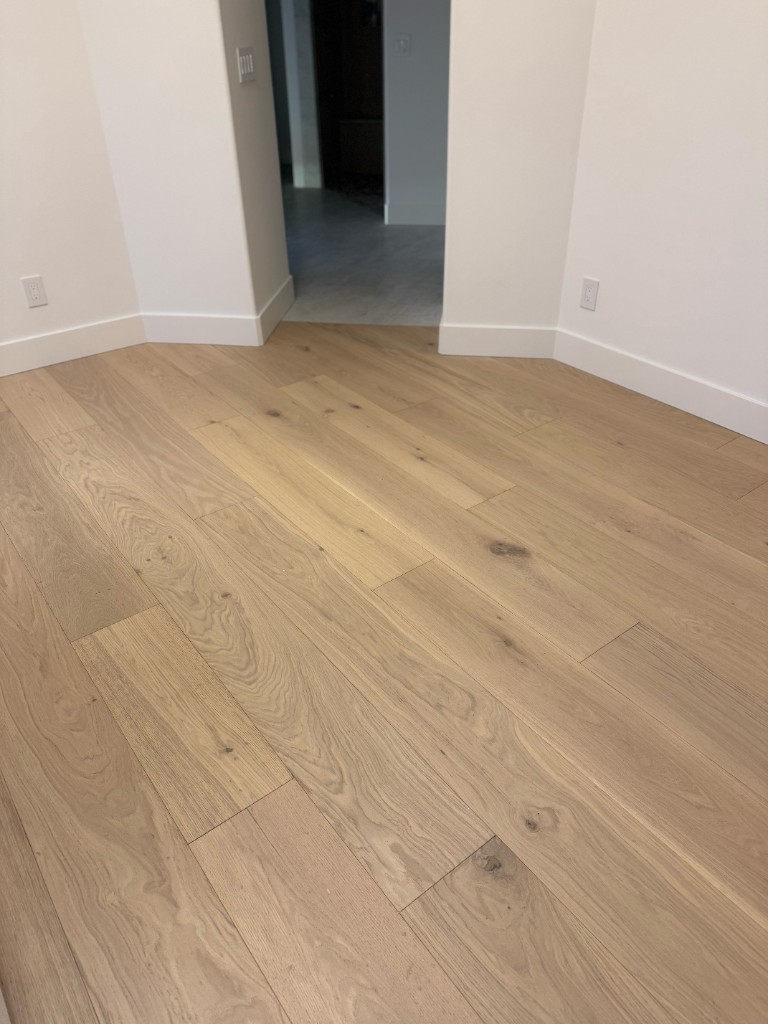 Professional installation of wide-plank light oak hardwood flooring in a modern home with white walls and baseboards