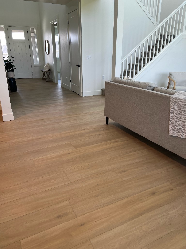 Light oak laminate or LVP flooring in modern open-concept living area with entryway and staircase