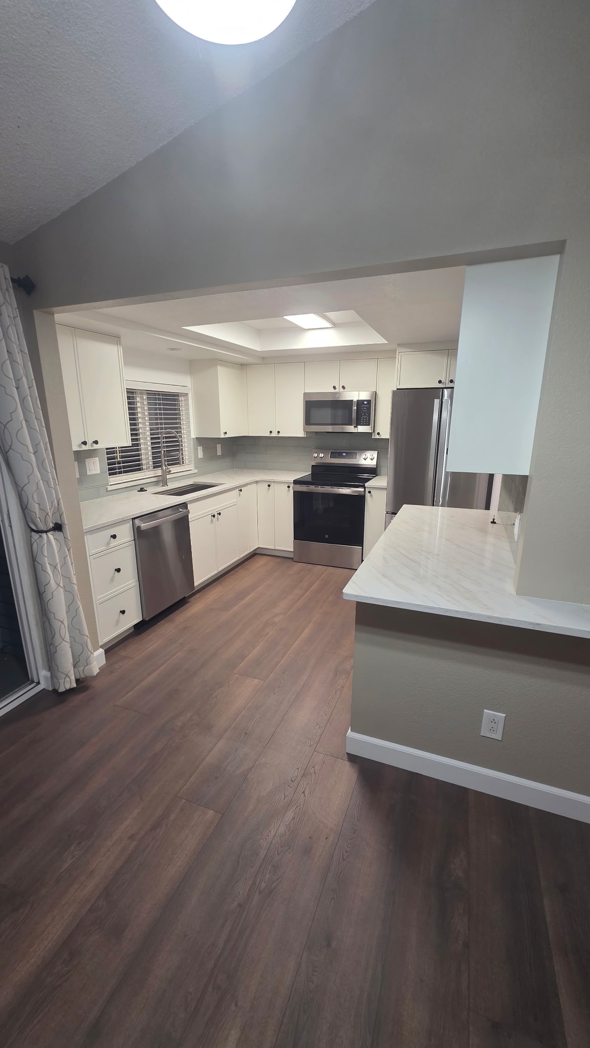 Modern kitchen with white shaker cabinets, stainless steel appliances, and dark wood-look flooring