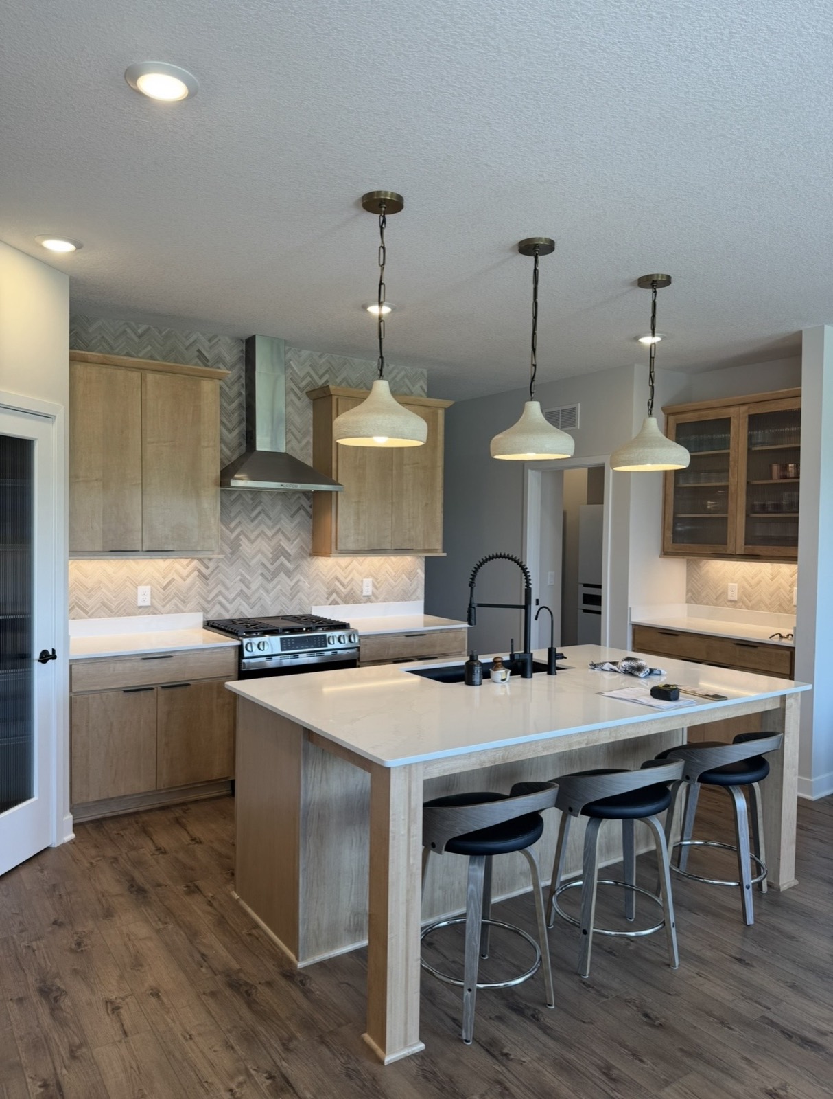 Modern kitchen with light wood cabinetry, large island, herringbone tile backsplash, and pendant lights