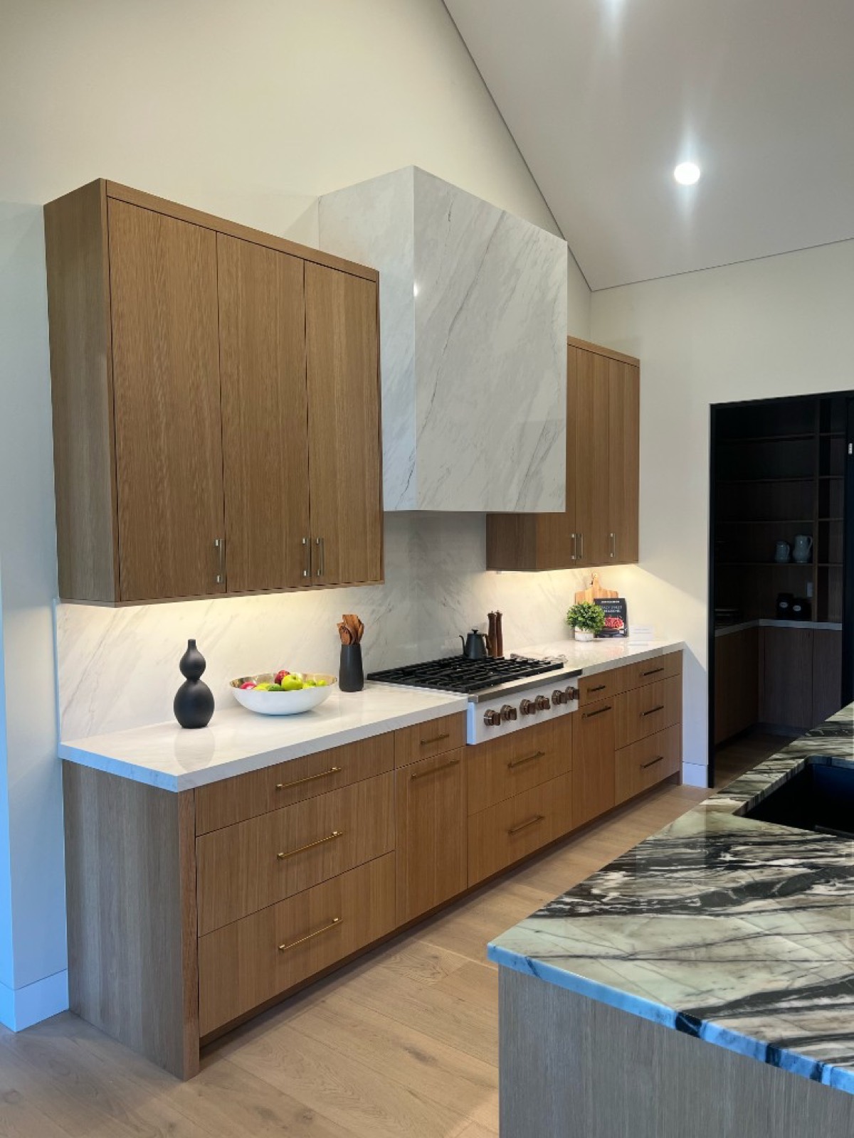 Kitchen remodel with light oak flat-panel cabinets, marble backsplash, and custom marble-clad range hood