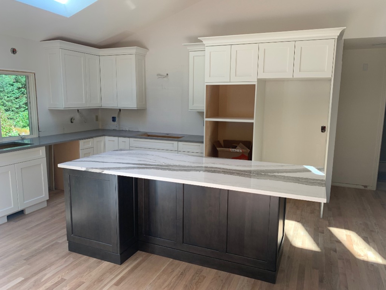 Kitchen renovation showing white shaker perimeter cabinets, dark island, and marble-look island countertop