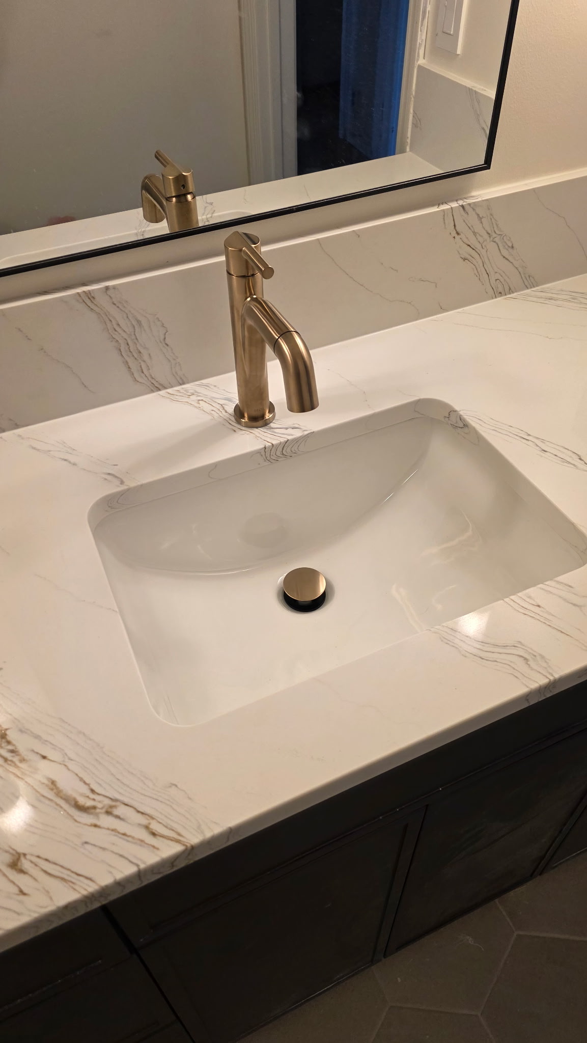 Bathroom vanity detail with white marble-look quartz countertop, undermount sink, and brushed gold faucet and drain